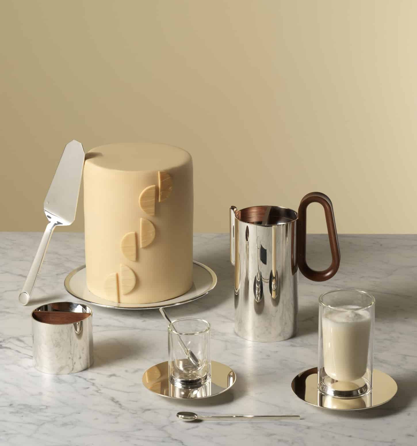 Mise en scène de la théière et du sucrier en métal argenté à côté de tasses de la collection Phi photographiés avec un gâteau sur un fond jaune clair