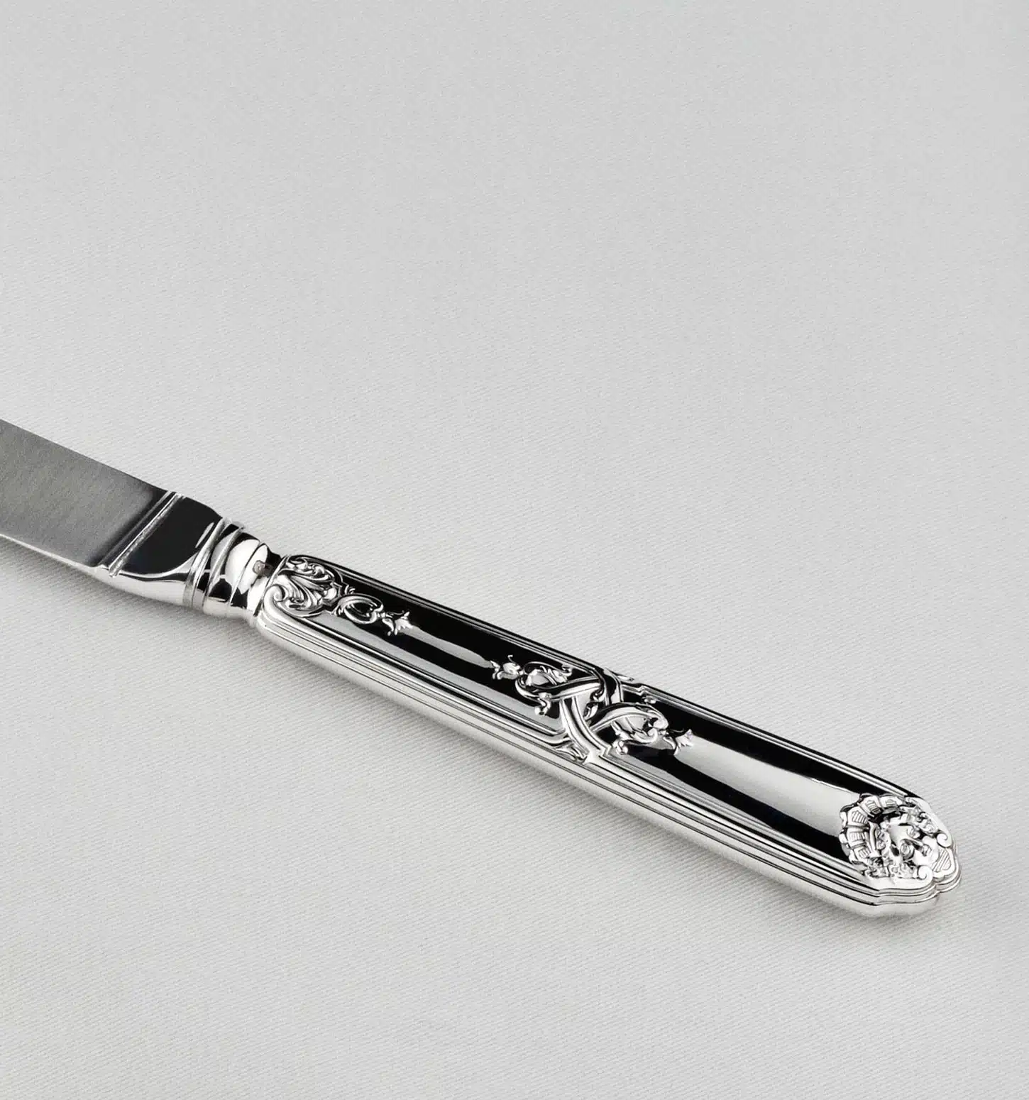 Manche de couvert de la collection Molière Mascaron en argent massif posé sur une nappe grise