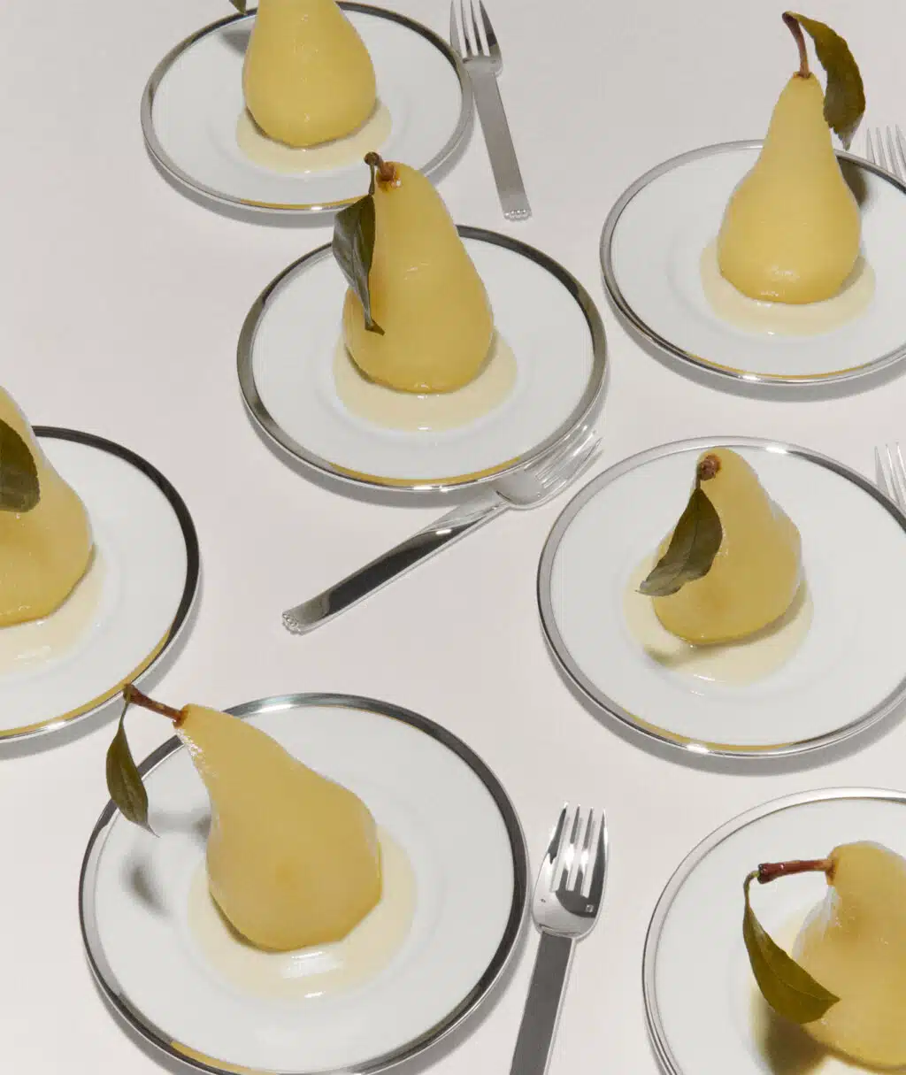 Assiettes Cercle  d'Orfèvre et fourchettes Deauville dressées avec des poires pochées sur une nappe blanche 